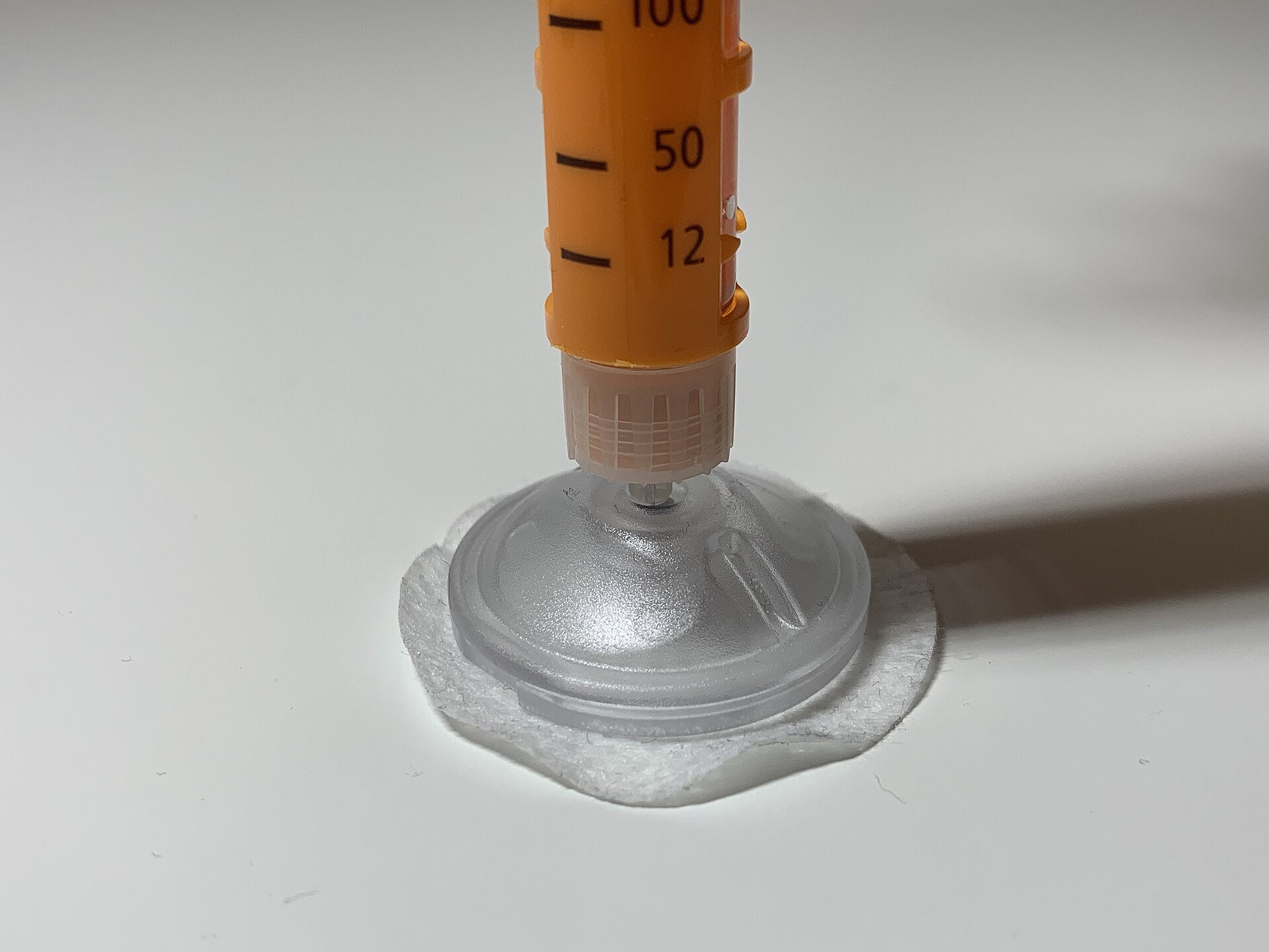 An injection pen held against a skin port on a forearm.